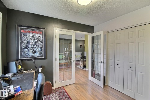 Room featuring wood-finish flooring, a pair of bi-fold closet doors with black hardware, and double French doors with clear glass panes - 30 14620 26 Street, Edmonton, AB 