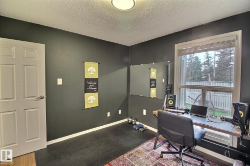 Room featuring a large window with privacy blinds, dark wall paint, textured ceiling, a flush mount ceiling light, and a white interior door - 30 14620 26 Street, Edmonton, AB 