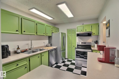 Bright kitchen featuring vibrant cabinetry, stainless steel appliances, a dual basin sink, ample countertop space, and checkerboard floor tiling - 30 14620 26 Street, Edmonton, AB 