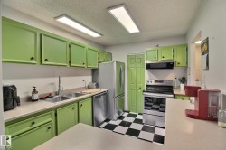 Bright kitchen featuring vibrant cabinetry, stainless steel appliances, a dual basin sink, ample countertop space, and checkerboard floor tiling - 