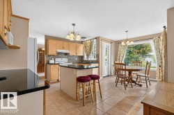 Kitchen featuring a central island with a dark countertop, light-toned cabinetry, tile flooring, and a mosaic tile backsplash - 