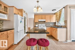 Kitchen featuring a central island with a dark countertop, light wood cabinetry, a tile backsplash, and light-toned floor tiles - 