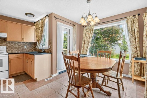 Kitchen and dining area featuring tile flooring, light wood-finish cabinetry, a tiled backsplash, and a contemporary pendant light fixture - 572 Byrne Crescent, Edmonton, AB 
