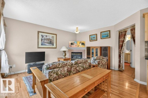Living area with wood-finish flooring, a fireplace with a stone surround, and light-toned walls - 572 Byrne Crescent, Edmonton, AB 