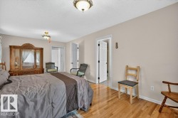 Spacious room featuring wood-finish flooring, two ceiling-mounted light fixtures, white baseboard trim, and a white interior door with black hardware - 