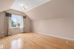 Spacious room featuring hardwood flooring, sloped ceilings, and a large multi-pane window - 