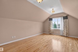 Spacious room featuring wood-finish flooring, a vaulted ceiling with two ceiling-mounted light fixtures, a large window with white trim, and neutral-toned walls - 