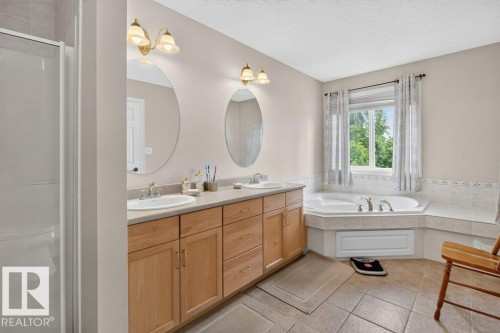 Bathroom featuring a dual vanity with light wood cabinetry, a built-in corner soaking tub, a separate glass-enclosed shower, and tile flooring - 572 Byrne Crescent, Edmonton, AB 