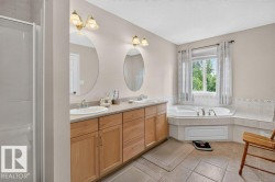 Bathroom featuring a dual vanity with light wood cabinetry, a built-in corner soaking tub, a separate glass-enclosed shower, and tile flooring - 