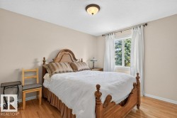 Bright bedroom featuring wood-finish flooring, a double-paned window with white draperies, and neutral-toned wall paint - 