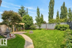 Expansive backyard featuring a stone paver pathway, mature trees, a wooden pergola, and a privacy fence - 