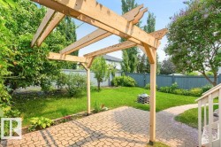 Expansive backyard featuring a natural wood pergola over a paver patio, a lush green lawn, mature trees, and a gravel pathway - 