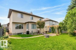 Expansive backyard featuring a manicured lawn, a wooden deck, a pergola with climbing greenery, and a paved patio area - 