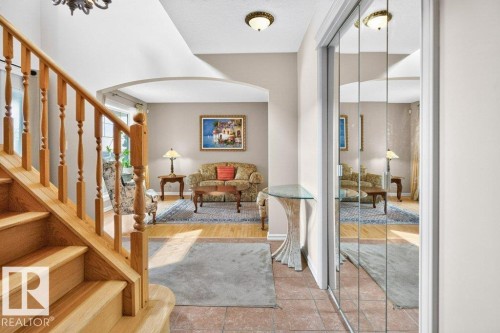 Entryway featuring a natural wood staircase, tiled flooring, mirrored closet doors, and an arched doorway leading to a living area with wood-finish flooring - 572 Byrne Crescent, Edmonton, AB 