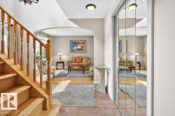 Entryway featuring a natural wood staircase, tiled flooring, mirrored closet doors, and an arched doorway leading to a living area with wood-finish flooring - 