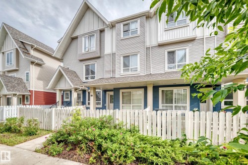 Modern townhome exterior featuring multi-level construction, durable siding, a pitched roofline, white picket fencing, and mature landscaping - 37 13003 132 Avenue Nw, Edmonton, AB 