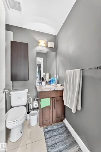 Bathroom featuring a wood-finish vanity with a stone countertop, an undermount sink, and a wall-mounted mirror - 37 13003 132 Avenue Nw, Edmonton, AB 