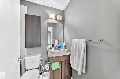 Bathroom featuring a vanity with a stone-finish countertop, wood-finish cabinetry, a wall-mounted mirror, and overhead lighting - 37 13003 132 Avenue Nw, Edmonton, AB 