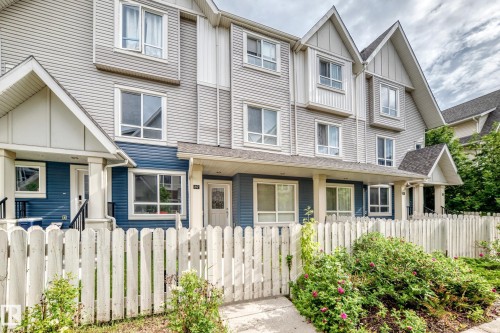 Multi-story townhome exterior featuring light gray horizontal siding, dark blue accent siding, white trim, and a white picket fence - 37 13003 132 Avenue Nw, Edmonton, AB 