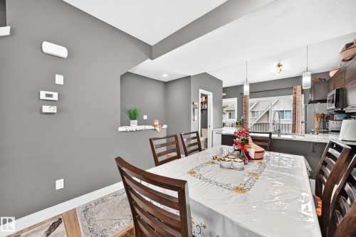 Open-concept dining area featuring wood-finish flooring, a pass-through window, and contemporary pendant lighting - 37 13003 132 Avenue Nw, Edmonton, AB 