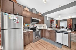 Open-concept kitchen featuring wood-finish flooring, stainless steel appliances, stone-finish countertops, dark wood cabinetry, and pendant lighting - 