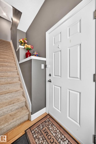 Entryway featuring a paneled door, wood-finish flooring, and a carpeted staircase - 37 13003 132 Avenue Nw, Edmonton, AB 