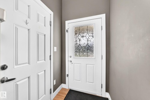 Entryway featuring a white paneled door with decorative leaded glass, wood-finish flooring, and neutral wall paint - 37 13003 132 Avenue Nw, Edmonton, AB 