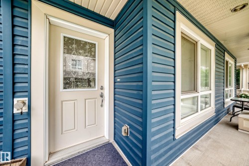 Entryway featuring a decorative glass panel door, blue horizontal siding, white trim, and a covered porch with concrete flooring - 37 13003 132 Avenue Nw, Edmonton, AB 