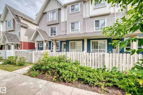 Townhouse exterior featuring a white picket fence, mature landscaping, and a concrete walkway - 37 13003 132 Avenue Nw, Edmonton, AB 