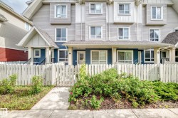 Townhome exterior featuring blue and gray siding, multiple windows, and a white picket fence - 