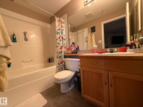 Bathroom featuring a built-in tub and shower combination, a wood-finish vanity with cabinet storage, and a large wall-mounted mirror - 205 3425 19 Street, Edmonton, AB 