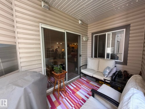 Covered patio featuring tan vinyl siding, a sliding glass door, and a window with dark trim - 205 3425 19 Street, Edmonton, AB 