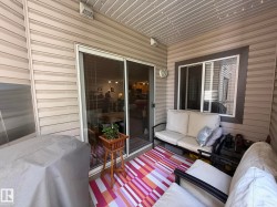 Covered patio featuring tan vinyl siding, a sliding glass door, and a window with dark trim - 