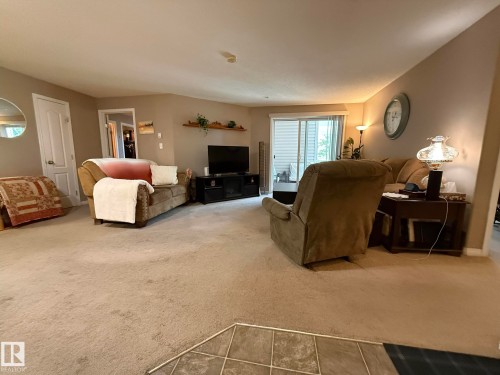 Spacious living area featuring neutral carpeting, light-toned walls, and a sliding glass door leading to an outdoor space - 205 3425 19 Street, Edmonton, AB 