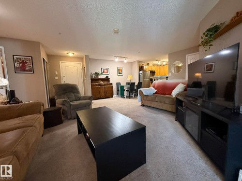 Open-concept living area featuring neutral carpet flooring, recessed lighting, and a kitchen with wood-finish cabinetry - 205 3425 19 Street, Edmonton, AB 