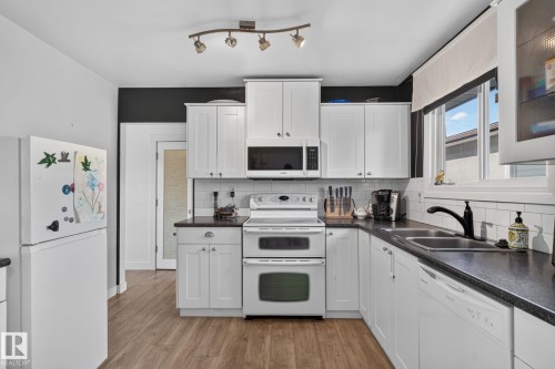 Kitchen featuring white cabinetry, dark countertops, white subway tile backsplash, and wood-finish flooring - 7803 73 Street, Edmonton, AB 