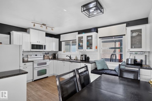 Kitchen featuring white shaker cabinetry, dark countertops, white subway tile backsplash, wood-finish flooring, and built-in window seating - 7803 73 Street, Edmonton, AB 