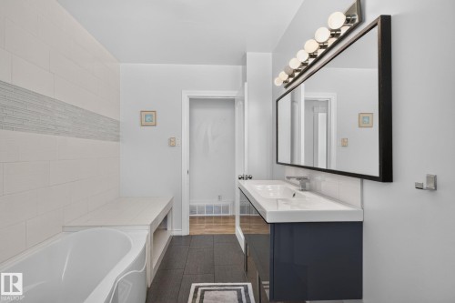 Bathroom featuring a contemporary vanity with an integrated sink, a rectangular framed mirror, and a linear light fixture with multiple bulbs - 7803 73 Street, Edmonton, AB 