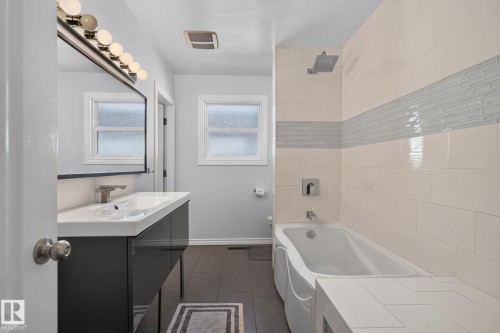 Contemporary bathroom featuring a dark vanity with an integrated white sink, a wall-mounted faucet, and a large mirror with overhead lighting - 7803 73 Street, Edmonton, AB 