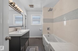 Contemporary bathroom featuring a dark vanity with an integrated white sink, a wall-mounted faucet, and a large mirror with overhead lighting - 