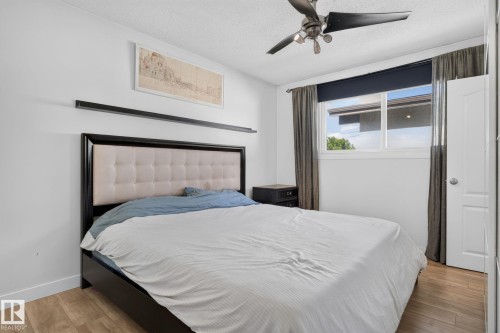 Bedroom featuring light wood-finish flooring, a contemporary ceiling fan, and a double window with a dark roller blind - 7803 73 Street, Edmonton, AB 