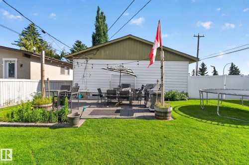 Expansive backyard featuring a stone paver patio, a lush green lawn, a white privacy fence, and mature trees - 7803 73 Street, Edmonton, AB 