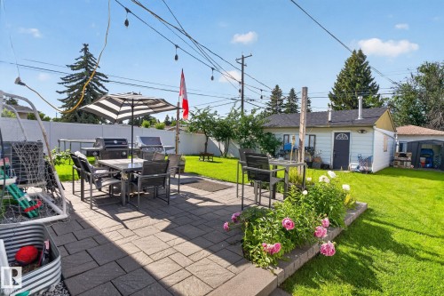 Expansive backyard featuring a paver patio with a raised flower bed, lush green lawn, and privacy fencing - 7803 73 Street, Edmonton, AB 