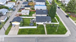 Corner lot property featuring a single-story residence with dark shingle roofing, a well-maintained front lawn, and a concrete pathway - 