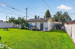 Expansive backyard featuring a large green lawn, perimeter fencing, mature trees, and a detached structure with a dark entry door - 