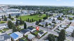 Aerial perspective showcasing a residential street with detached homes, mature trees, and a green space - 