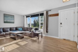 Open-concept living area featuring wood-finish flooring, a large picture window with outdoor scenery, light gray wall paint, and a white entry door with a digital lock - 