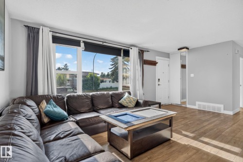 Living area featuring large picture windows, wood-finish flooring, white baseboards, a white entry door with security hardware, and a built-in mirrored closet door - 7803 73 Street, Edmonton, AB 