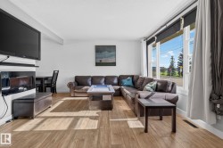 Living area featuring wood-finish flooring, a large window with white framing, and a wall-mounted television above a built-in electric fireplace unit - 
