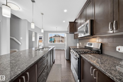Kitchen featuring an expansive island with an undermount sink, granite-style countertops, dark wood cabinetry, stainless steel appliances, and wood-finish flooring - 2331 Casey Crescent Sw, Edmonton, AB 